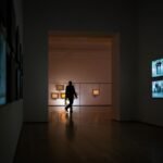 Silhouette of a man walking through a dimly lit art gallery surrounded by illuminated screens.