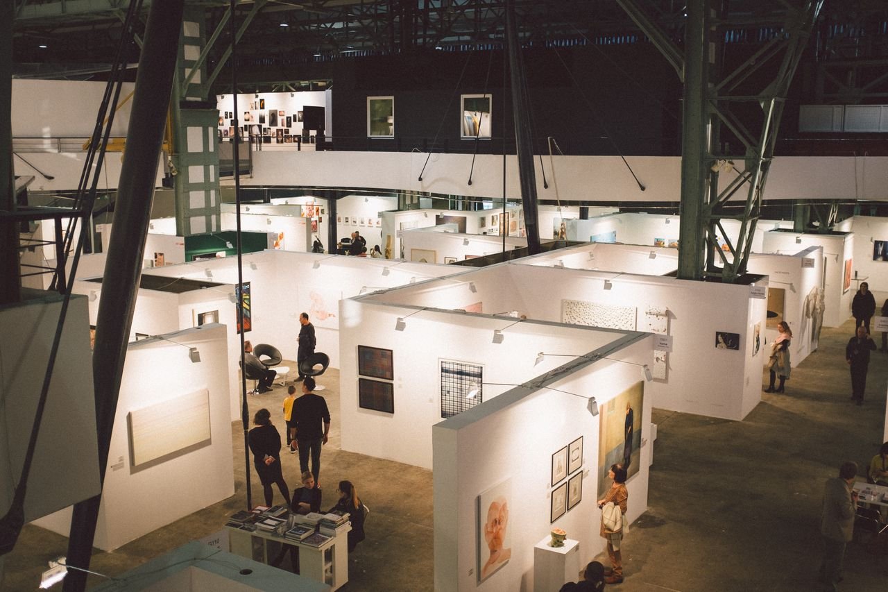 Art exhibition showcasing diverse paintings and installations in a spacious Budapest gallery.